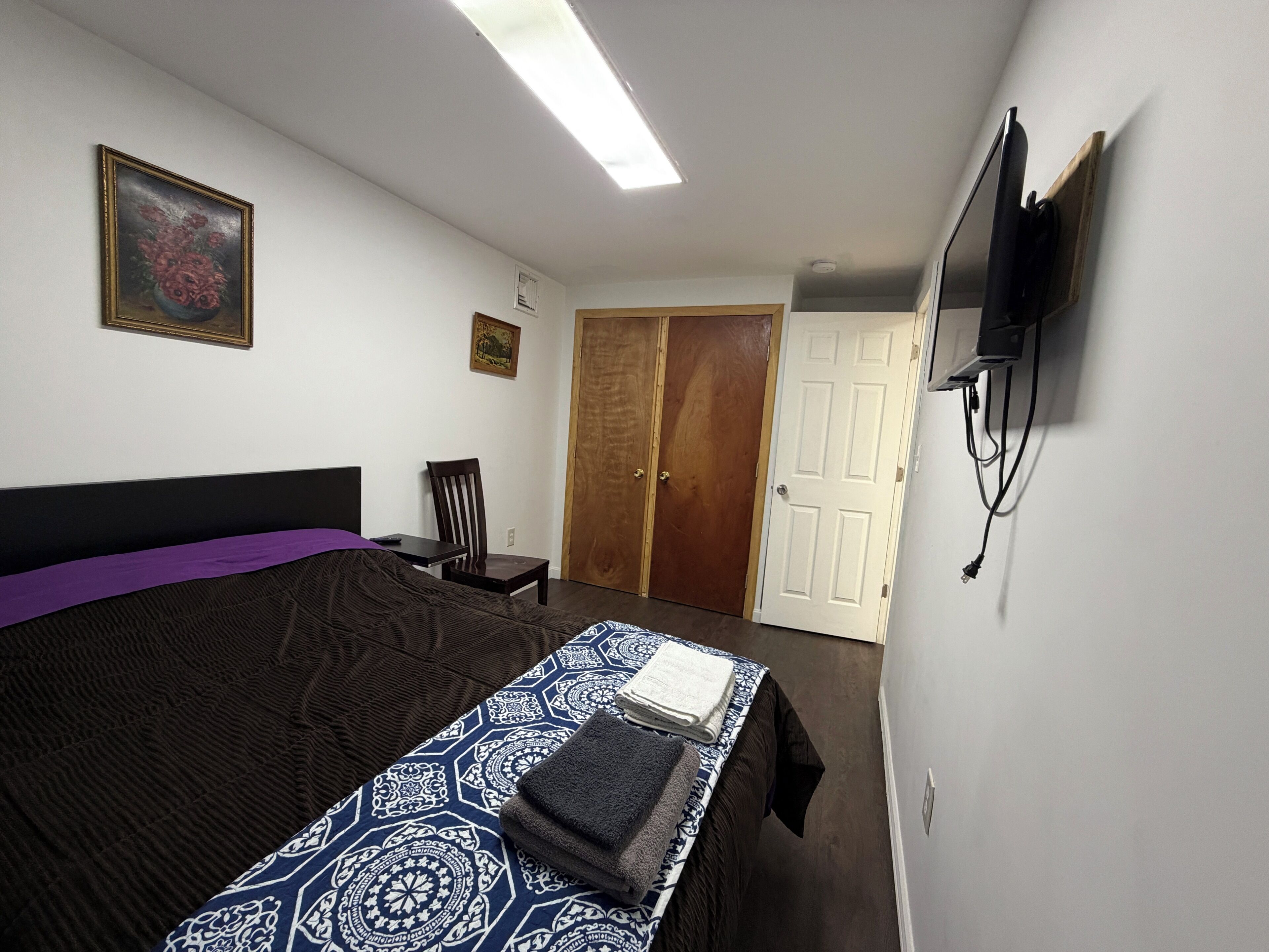 A bedroom with a bed, a chair, a TV mounted on the wall, and a door.