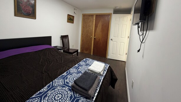 Ein Schlafzimmer mit einem Bett, einem Sessel, einem an der Wand montierten Fernseher und einer Tür.