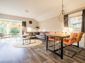 Ein modernes Wohnzimmer mit Essbereich, einer Couch, einem Couchtisch und einer Pendelleuchte.