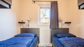 Une chambre avec deux lits, une fenêtre avec des rideaux, un radiateur et des lampes fixées au mur.