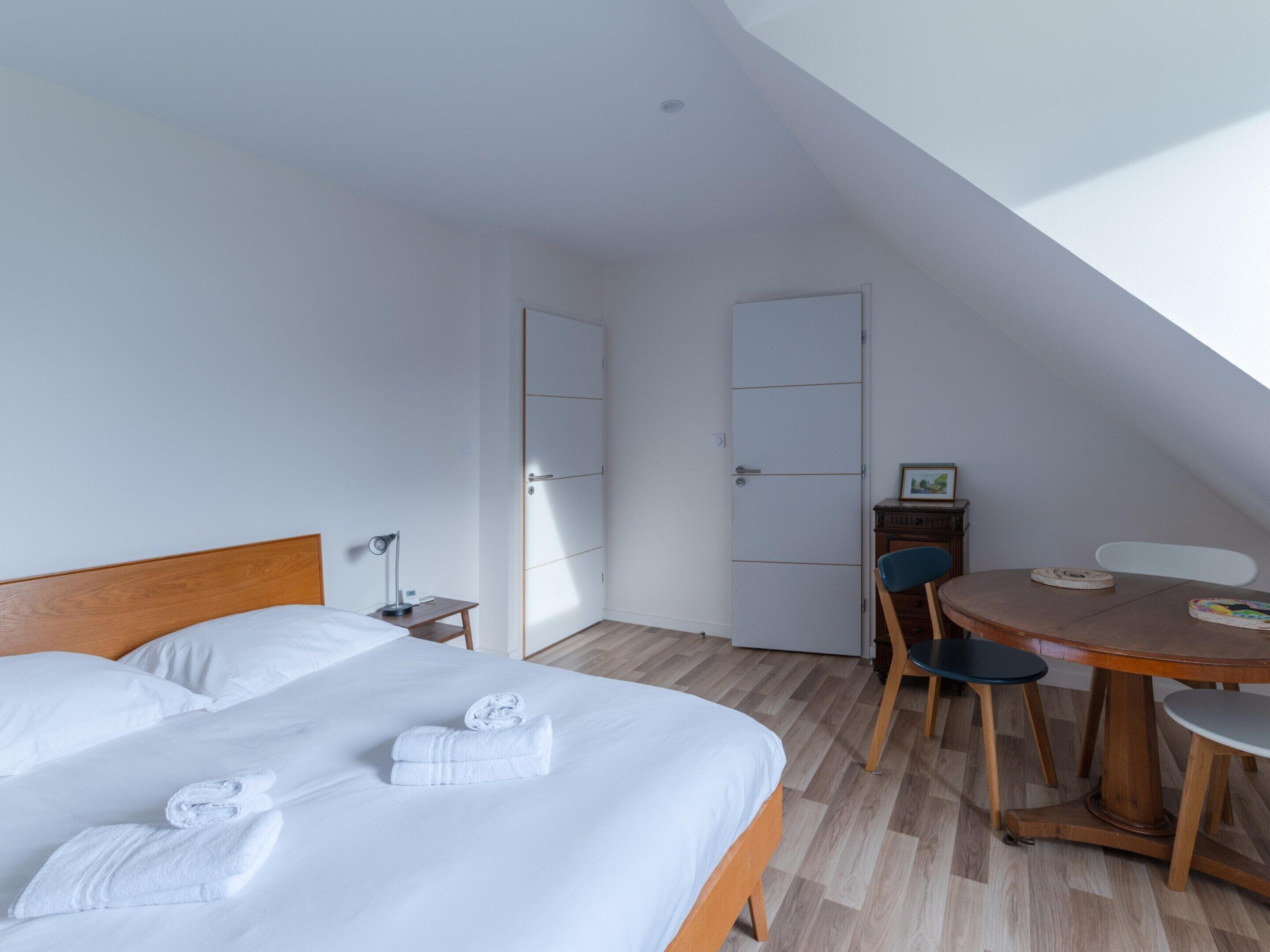 A hotel room with a bed, a small table with chairs, a desk, and a wardrobe.