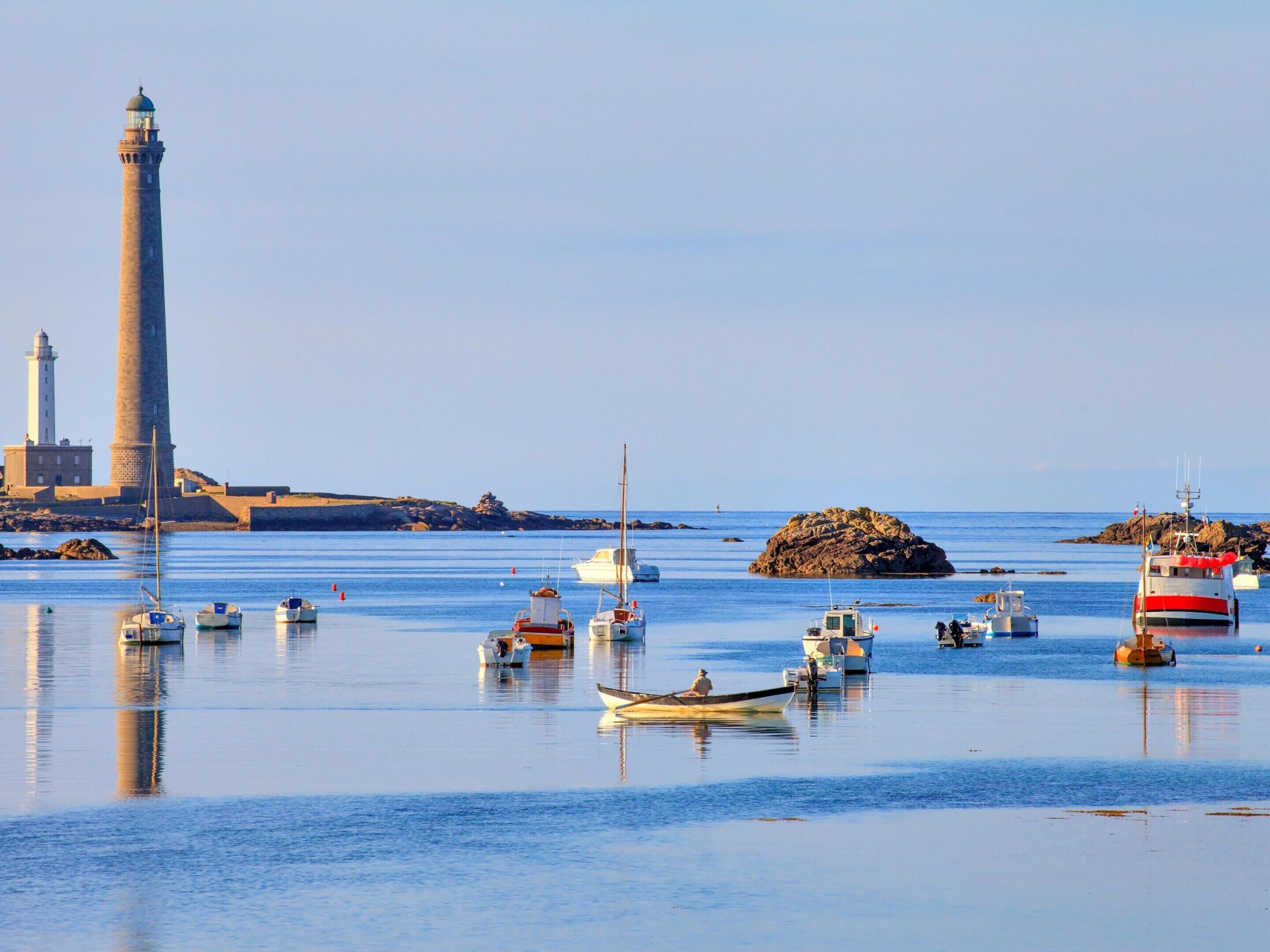 A coastal scene with a lighthouse, boats, and rocky outcrops.