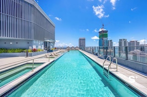 Ein Pool auf dem Dach mit klarem, blauem Wasser, umgeben von modernen Gebäuden und einer Stadtansicht.