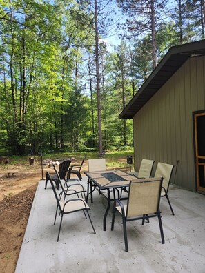 An outdoor patio with a table and chairs, surrounded by a forest. - Up North Cottage/ ORV Trail with in minutes (Kalkaska)