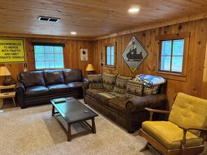 A wooden interior with a brown leather sofa, a patterned sofa, a small table, and a yellow armchair. - Up North Cottage/ ORV Trail with in minutes (Kalkaska)