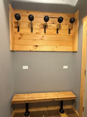 Eine hölzerne Bank mit Metallgestell, ein an der Wand befestigter Kleiderhaken mit fünf Haken und zwei Steckdosen an der Wand.