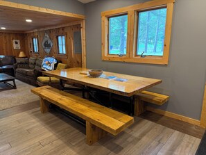 A wooden interior with a dining table, benches, a sofa, and a window with a view of trees. - Up North Cottage/ ORV Trail with in minutes (Kalkaska)