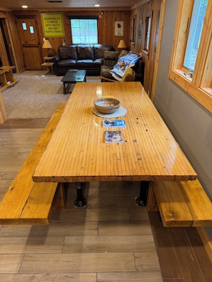 Puinen ruokapöytä penkeillä, nahkasohva ja ikkuna, josta avautuu näkymä puihin.