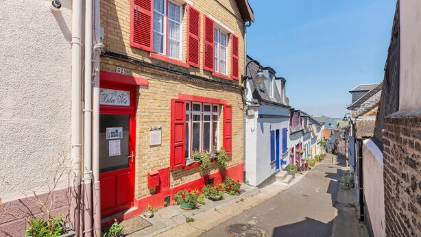A narrow street with buildings featuring red shutters and a sign for 'Dole Vita.' - Courtgain Guest Rooms in Saint-Valery-sur-Somme (Saint-Valery-sur-Somme)