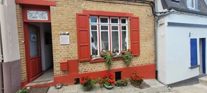 A brick building with red shutters, a sign reading 'Dolce Vita,' and potted plants at the entrance.