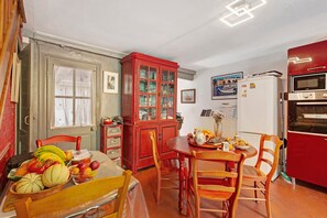 A dining area with a table set for two, a red cabinet with glass doors, a white refrigerator, and a red oven.