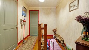 A hallway with a patterned carpet, a wooden bench, a small table with a vase of flowers, and a framed picture on the wall. - Courtgain Guest Rooms in Saint-Valery-sur-Somme (Saint-Valery-sur-Somme)