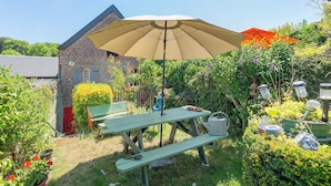 A garden with a picnic table, a large umbrella, and a brick building. - Courtgain Guest Rooms in Saint-Valery-sur-Somme (Saint-Valery-sur-Somme)