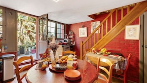 A dining area with a round wooden table, chairs, and a red brick wall. - Courtgain Guest Rooms in Saint-Valery-sur-Somme (Saint-Valery-sur-Somme)
