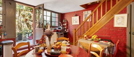 A dining area with a round wooden table, chairs, and a red brick wall.