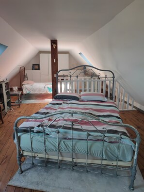 A room with a sloped ceiling, a metal bed frame, a wooden floor, and a white wardrobe.