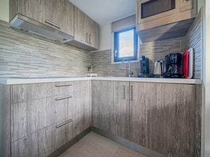Eine moderne Küche mit Holzschränken, einer Edelstahl-Dunstabzugshaube, einem Fenster und einer Kaffeemaschine.