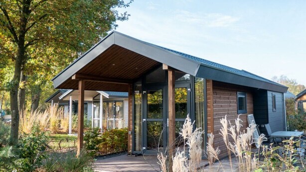 Une maison moderne dotée d’un porche abrité, d’une façade en briques et d’un jardin planté de hautes herbes.