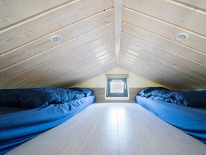 Ein kleines Schlafzimmer im Dachgeschoss mit zwei Betten, einem Oberlicht und einer Holzzielung.