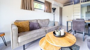 Un salon moderne comprenant un canapé, une table basse ronde en bois, un coin repas avec une table et des chaises, et un appareil de climatisation fixé au mur.