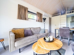 Ein modernes Wohnzimmer mit einer Couch, einem runden Holztisch, einem Essbereich mit Tisch und Stühlen sowie einer Wand-Klimaanlage.