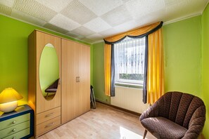 A room with a large wardrobe, a chair, a window with curtains, and a lamp. - Stoll Holiday Apartment in Brüel (Brüel)
