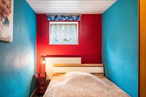A room with a bed, a radiator, a window with a blue curtain, and a wall with a red section. - Stoll Holiday Apartment in Brüel (Brüel)