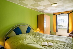 Ein Hotelzimmer mit Bett, Nachttisch, Lampe und einem fenster mit Vorhängen.