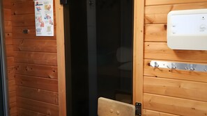Ein Holzblockhaus-Interieur mit einer Tür zu einem dunklen Raum, einem Wandheizgerät und einem kleinen Tisch mit einer Schüssel.