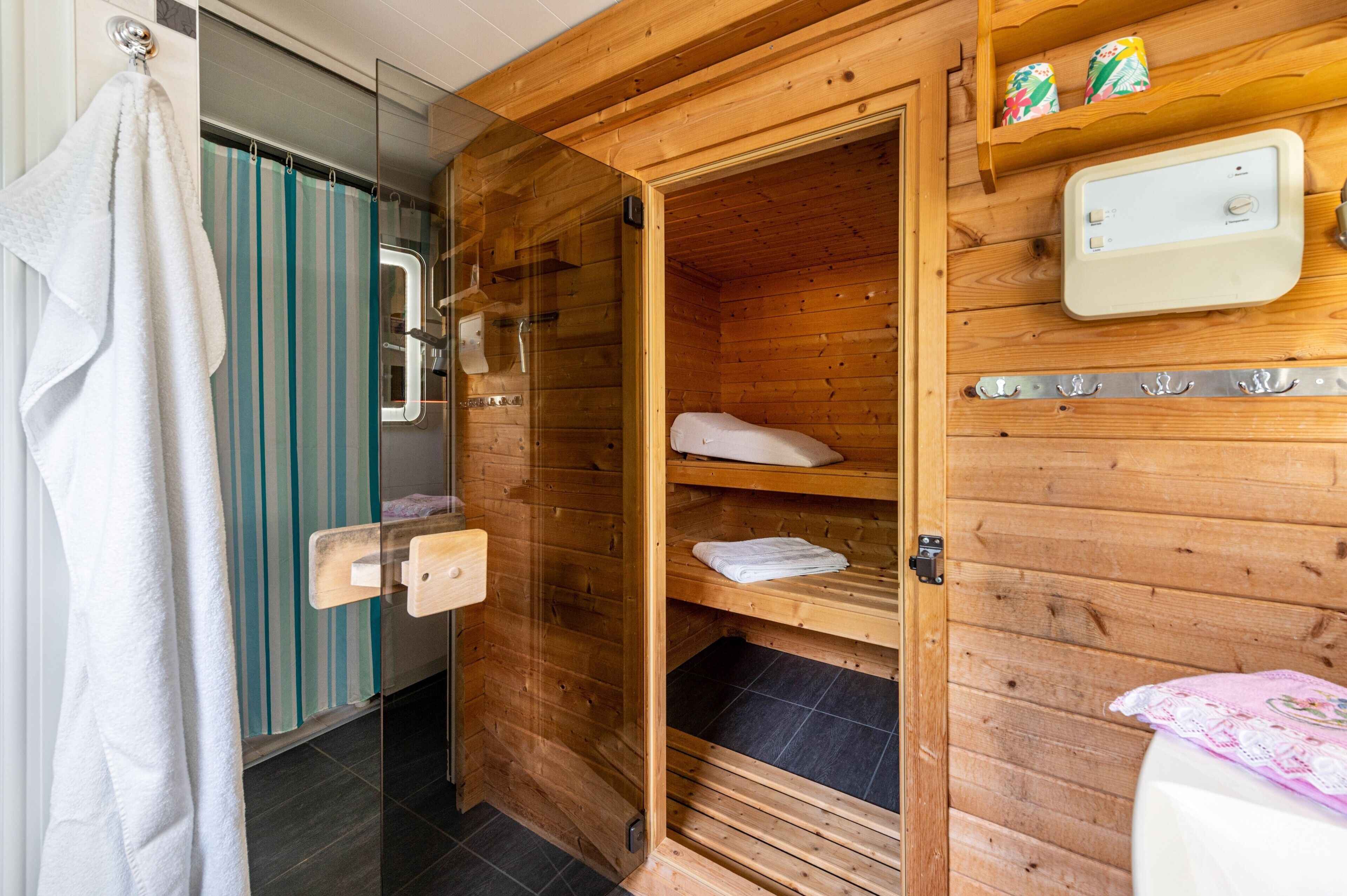 A wooden sauna room with a glass door, a towel rack, and a control panel.
