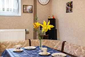 Ein Esstisch mit blauer Tischdecke, eine Vase mit gelben Blumen und eine Uhr an der Wand.