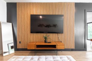 Ein modernes Wohnzimmer mit einem flachbildfernseher, der an einer Holzwand befestigt ist, einer Holz-Unterhaltungseinrichtung darunter und einem großen Fenster auf der rechten Seite.