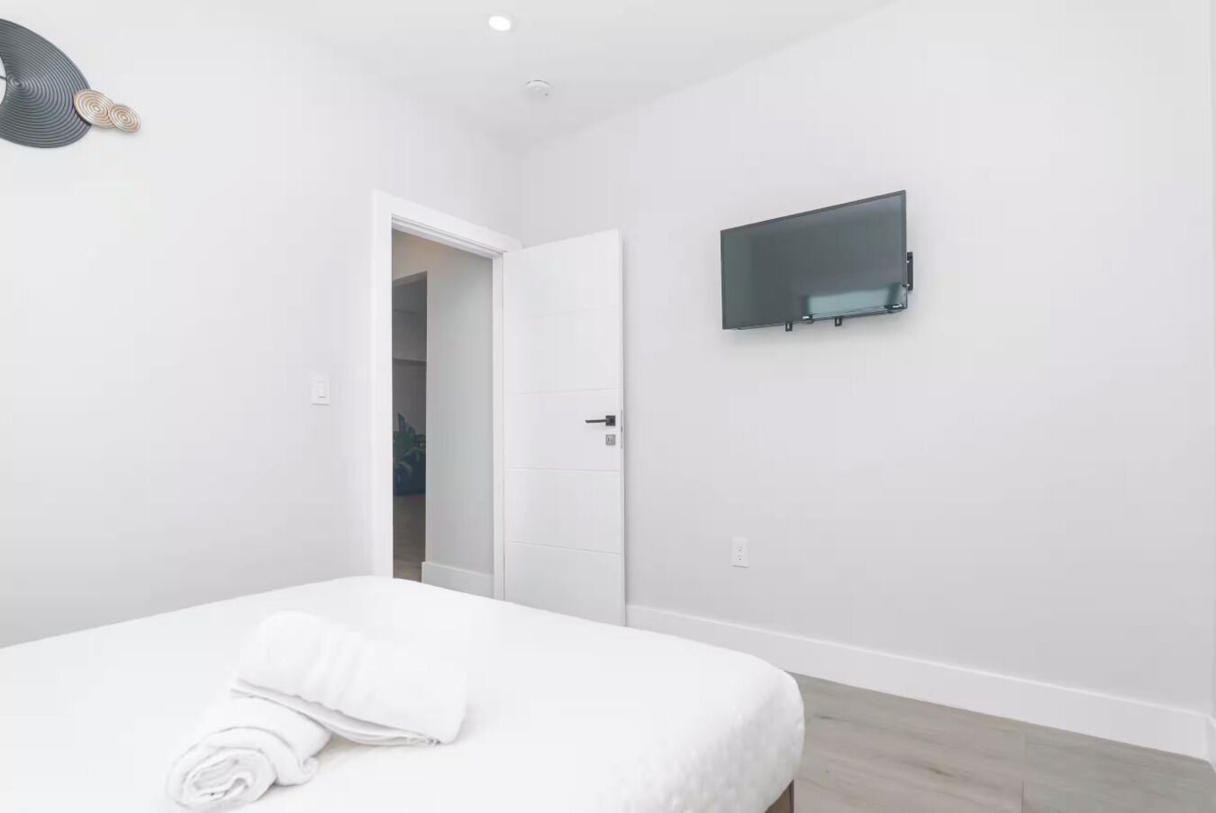 A bedroom with a bed, a TV mounted on the wall, and a door leading to another room.