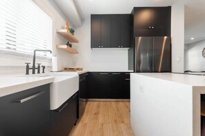 Eine moderne Küche mit schwarzen Schränken, einem Edelstahlkühlschrank und einer weißen Arbeitsplatte.