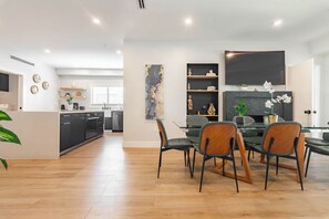 Una cocina moderna con armarios negros, un comedor con mesa y sillas de vidrio, y una sala de estar con chimenea.