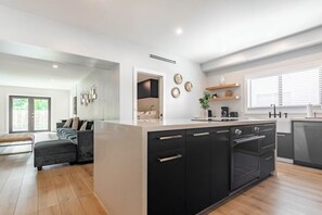 Una cocina moderna con una isla central, armarios negros y un área de comedor con sofá y banco.