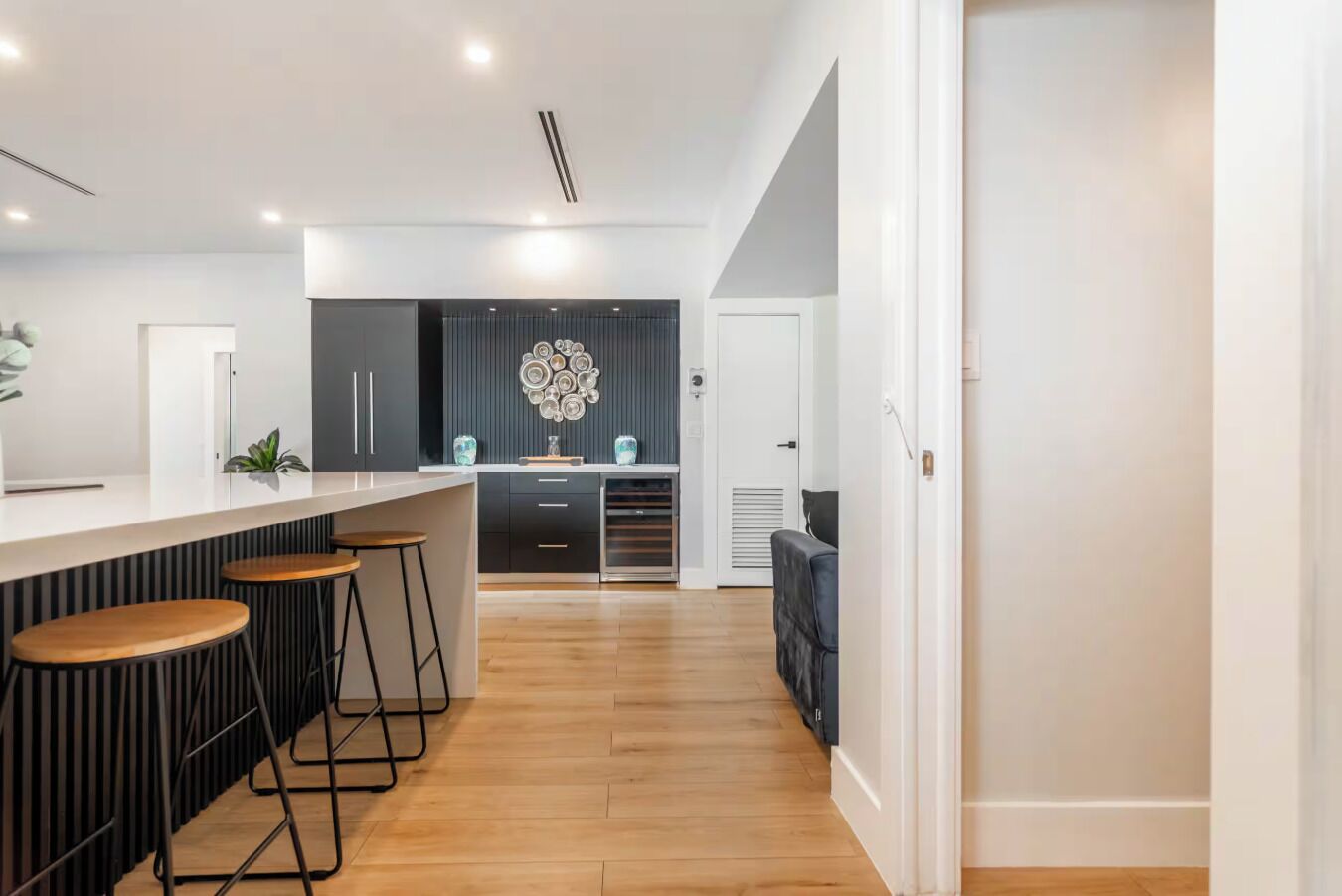 A modern kitchen with a central island, bar stools, and a decorative wall piece.