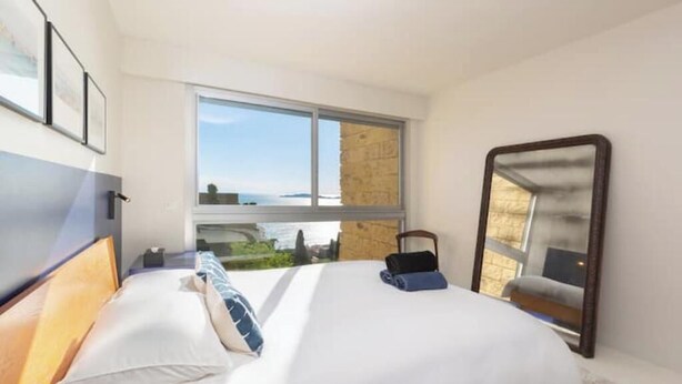 A hotel room with a bed, a window, a mirror, and a view of the outside. - An Endless Summer (Marseille)