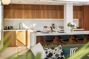 Une cuisine moderne avec des meubles en bois, un îlot central doté de tabourets de bar et un coin repas avec un canapé vert.
