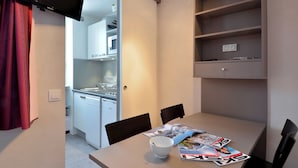 Ett kompakt kök med vita skåp, diskmaskin och en matplats med bord och stolar.