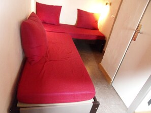 Ein kleines Zimmer mit einem Bett, einem kleinen Tisch, einer Tür und einer Lampe.