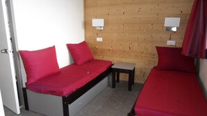 Ett litet rum med två sängar, ett litet bord och två vägglampor.