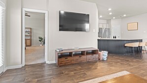 Ein modernes Wohnzimmer mit Flachbildfernseher an der Wand, einer Holz-Unterhaltungseinheit und einer Küchenzeile mit Theke.