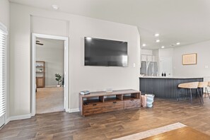 Ein modernes Wohnzimmer mit Flachbildfernseher an der Wand, einer Holz-Unterhaltungseinheit und einer Küchenzeile mit Theke.