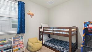 Ein Kinderzimmer mit Etagenbetten, einem Bücherregal, einem Sitzsack und einem Basketballkorb.