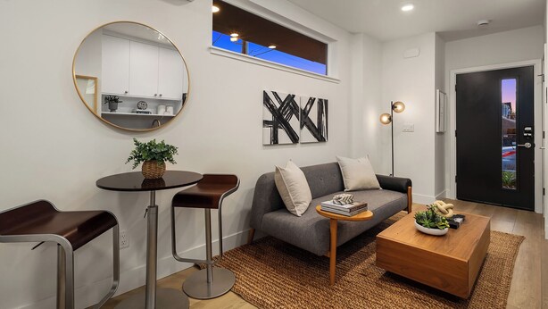 A modern living room with a grey sofa, round coffee table, and a small dining area with a round table and bar stools. - Charming studio in Seattle perfect for your city getaway (Seattle)