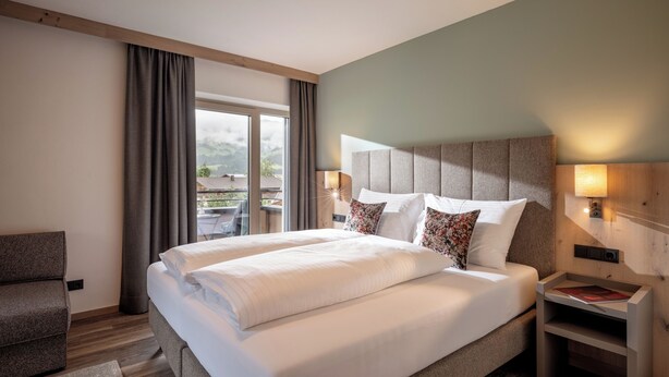 A hotel room with a large bed, a nightstand, a chair, and a view of the outdoors.