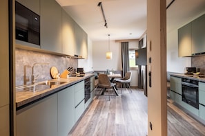 A modern kitchen with a built-in oven, a sink, and a dining area with chairs. - by franz - Alpine Apartments (Kirchberg in Tirol)