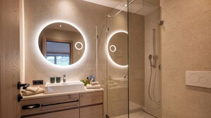 A modern bathroom with a glass-enclosed shower, a round mirror, and a wooden vanity.