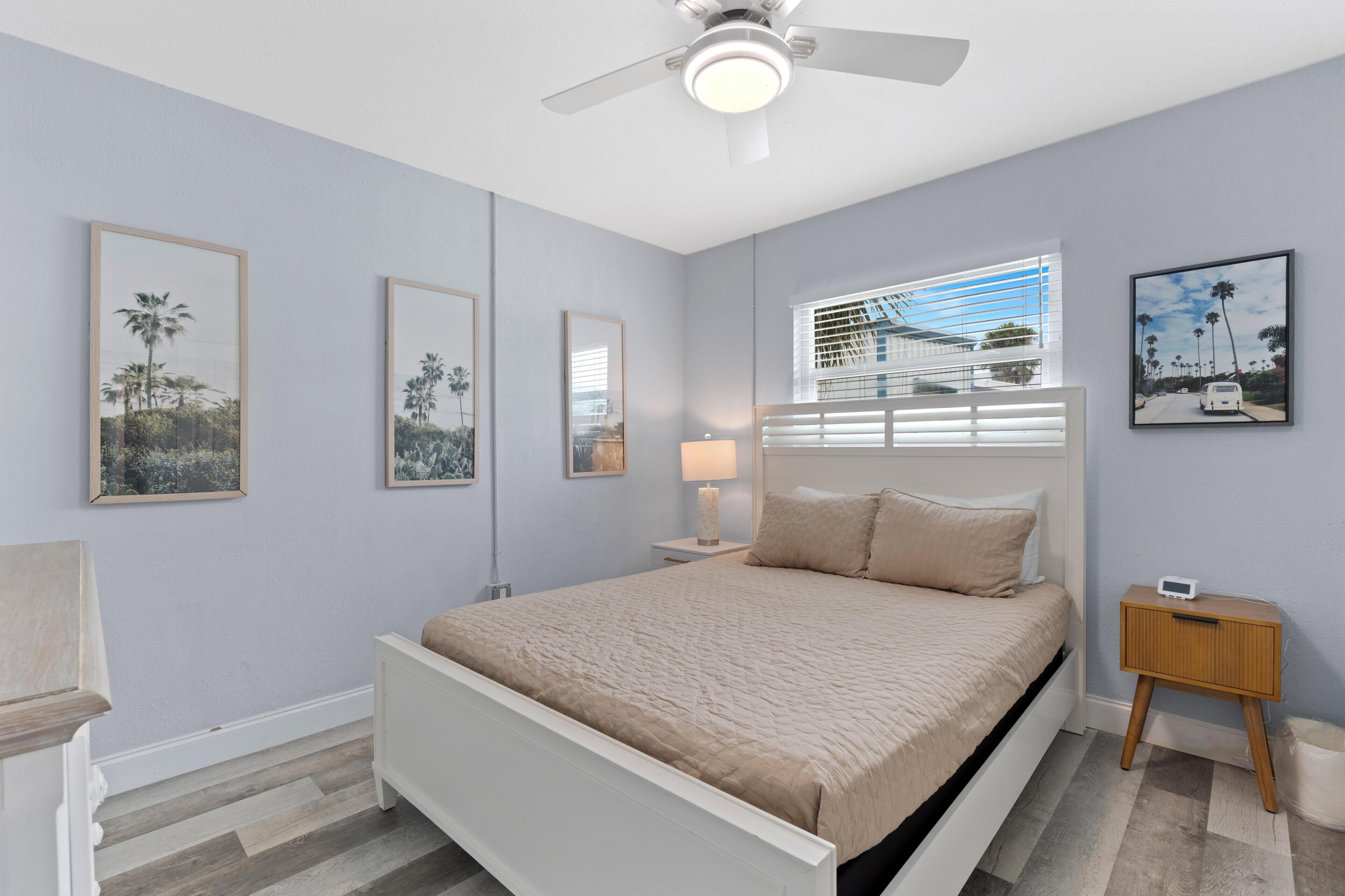 A bedroom with a bed, a nightstand, a ceiling fan, and framed pictures on the wall.